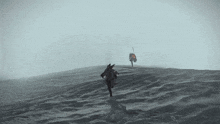 a couple of people standing on top of a hill in the middle of the ocean .