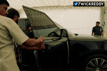 a man standing next to a black car with a twitter logo above him