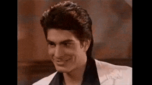 a young man in a white suit and black shirt is smiling .