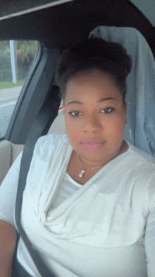 a woman in a white shirt is sitting in a car with a seat belt on