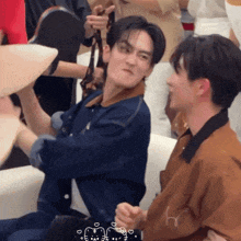 two men are sitting next to each other on a couch and one of them is making a face .