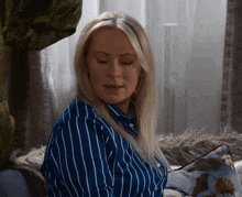 a woman wearing a blue and white striped shirt sits on a couch with her eyes closed