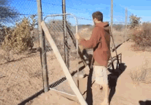 a man in a brown hoodie is standing next to a fence
