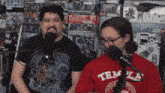 a man wearing a black shirt with a dragon on it and a woman wearing a red shirt that says temple on it