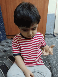 a young boy wearing a red and white striped shirt sits on the floor