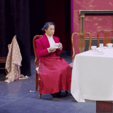 a woman in a red coat sits at a table holding a cup