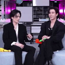 two men in suits are sitting next to each other on a couch and talking .