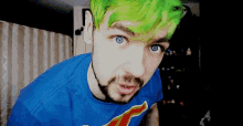 a man with green hair and a beard is wearing a blue shirt with a superhero on it .