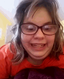 a girl wearing glasses and a red shirt smiles for the camera