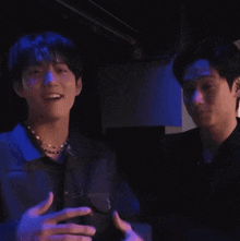 two men are standing next to each other in a dark room with purple lights .