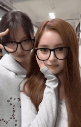 two girls wearing glasses are posing for a picture and one is wearing a sweatshirt with a zodiac sign on it