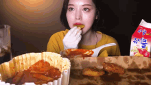 a woman in a yellow shirt is eating a piece of food next to a box of chicken