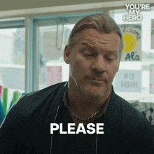 a man in a black jacket says please in front of a window