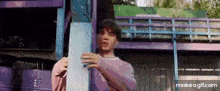 a man in a pink shirt is standing in front of a purple building holding a piece of wood .