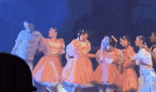 a group of young girls in orange dresses are dancing on a stage .