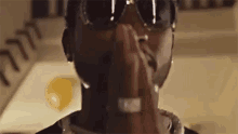 a close up of a man wearing sunglasses and a ring covering his face .