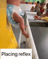 a baby in a diaper is standing next to a hospital bed and the word placing reflex is on the bottom