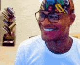 a man wearing glasses and a bandana smiles in front of a bookshelf