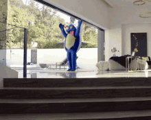 a person in a blue shark costume stands in front of a sliding glass door