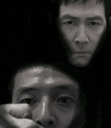 a black and white photo of a man 's face with another man 's face behind him