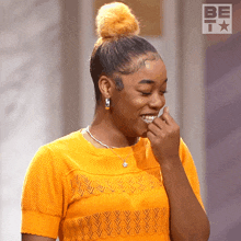 a woman wearing an orange shirt is smiling with a bet logo in the background