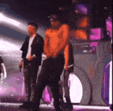 a man in an orange shirt is standing on a stage with other people