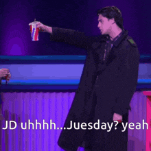 a man in a black coat is holding a cup that says ' jd uhhhh juesday yeah ' on it