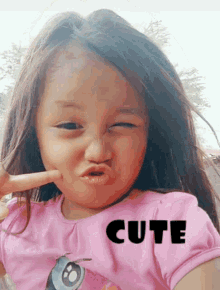 a little girl wearing a pink shirt with cute written on it