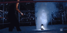 a man is walking into a wrestling ring with a lantern and smoke coming out of it .