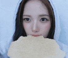 a woman wearing a white hoodie is holding a piece of bread in front of her face