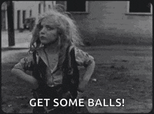 a little girl is making a funny face in a black and white photo and saying `` get some balls '' .