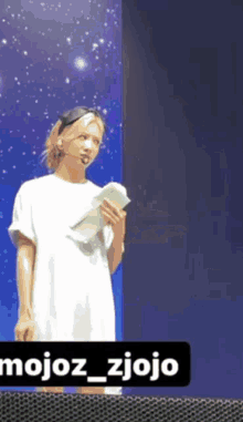 a man in a white shirt is standing in front of a blue wall with a sign that says mojoz_zjojo on it