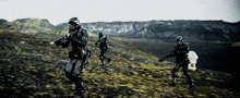 a group of soldiers are running across a field with mountains in the background