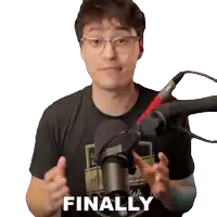 a man wearing glasses and a black shirt stands in front of a microphone and says " finally "