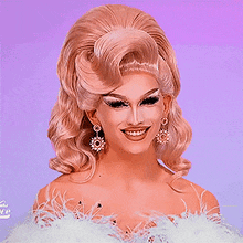 a drag queen wearing a feathered top and earrings smiles for the camera