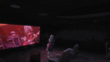 a girl stands in front of a large screen that shows a girl singing and playing a guitar