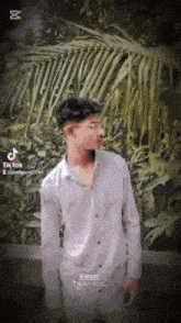 a young man wearing glasses and a white shirt is standing in front of a palm tree ..
