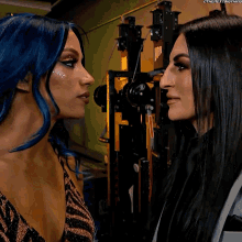 a woman with blue hair looks at another woman with black hair in a gym