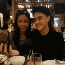 a man and a woman are sitting at a table taking a picture with a cell phone