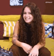 a woman is sitting on a couch with a guitar and smiling with gifsdayrol written below her
