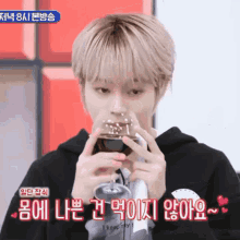a young man with blonde hair is drinking from a glass while wearing a black hoodie .