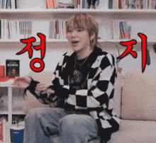 a man wearing a black and white checkered jacket is sitting on a couch holding a popcorn
