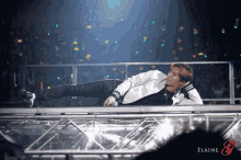 a man laying on a stage with elaine written on the bottom right corner
