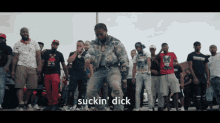 a man in a plaid jacket is dancing in front of a crowd and the word suckin ' dick is visible