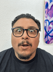 a man wearing glasses makes a funny face in front of a purple skateboard