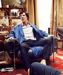 a man in a blue jacket sits in a chair in a room