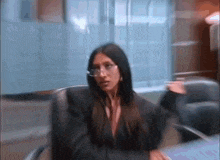 a woman wearing glasses and a suit is sitting in a chair in an office .
