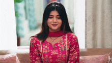 a woman is sitting on a couch wearing a pink dress and a necklace .