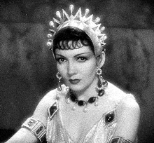 a black and white photo of a woman wearing a tiara , necklace , and bracelets .