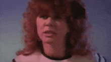 a woman with red hair and a white shirt is looking at the camera in a close up of her face .